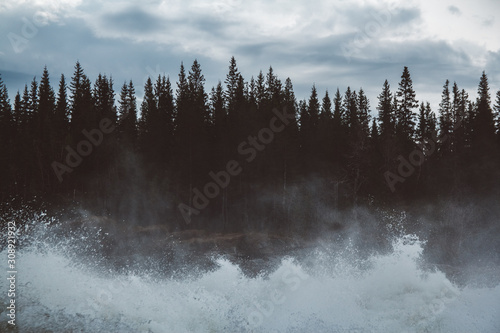 Waves and splashes of mountain river on background of forest, rocks and dramatic sky. Forest river water landscape. Wild river in mountain forrest panorama photo