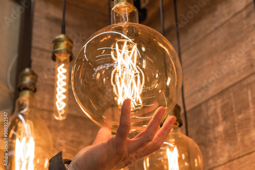 Burning huge incandescent edison lamps with a large decorative spiral in the man hand. Concept