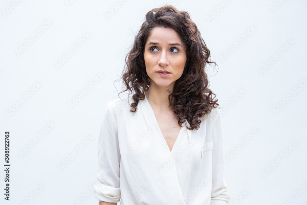 Pensive female customer looking up, studying copy space. Wavy haired young woman in casual shirt standing isolated over white background. Advertising concept Pensive female customer looking up, studying copy space. Wavy haired young woman in casual shirt standing isolated over white background. Advertising concept