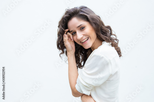 Happy joyful beautiful woman touching facial skin, laughing, looking at camera. Wavy haired young woman in casual shirt standing isolated over white background. Positive female portrait concept