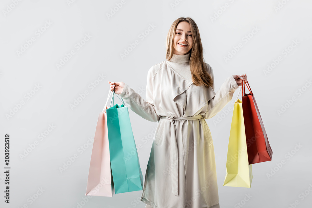 cheerful, stylish girl looking at camera while holding shopping bags isolated on grey cheerful, stylish girl looking at camera while holding shopping bags isolated on grey