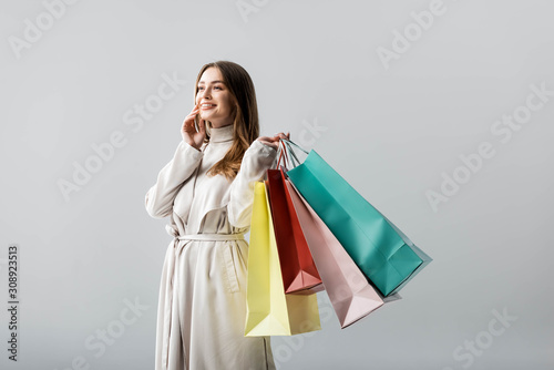 trendy girl looking away while holding shopping bags isolated on grey