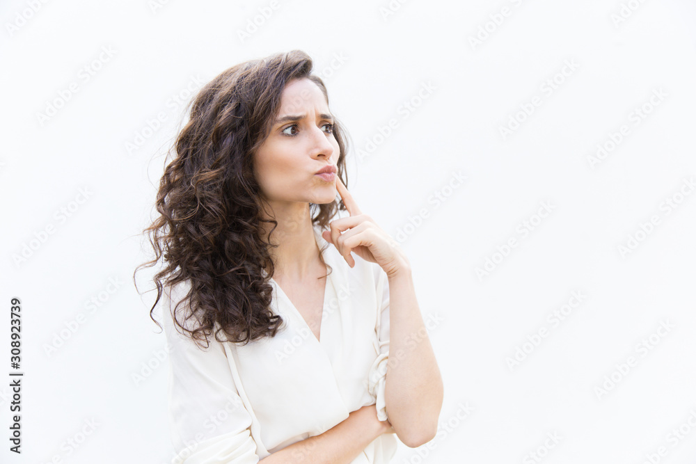 Focused pensive customer touching face with finger, looking away at copy space. Wavy haired young woman in casual shirt standing isolated over white background. Thinking or advertising concept Focused pensive customer touching face with finger, looking away at copy space. Wavy haired young woman in casual shirt standing isolated over white background. Thinking or advertising concept