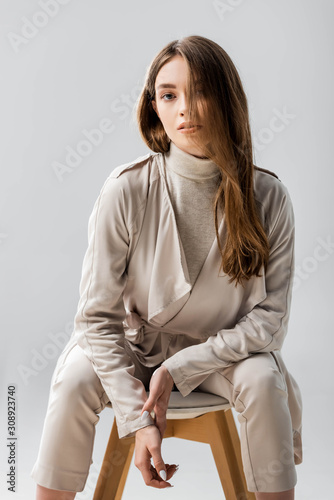 attractive, confident girl looking at camera while sitting on chair isolated on grey