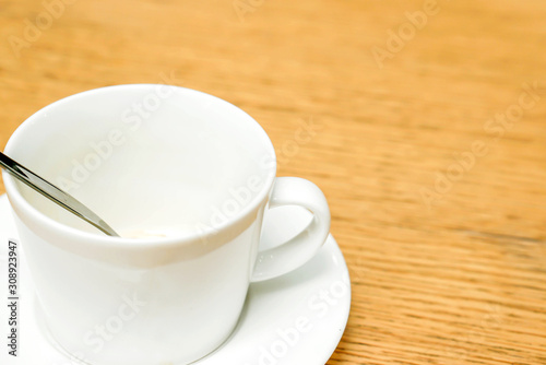 white coffee cup and spoon with saucer on wooden table.