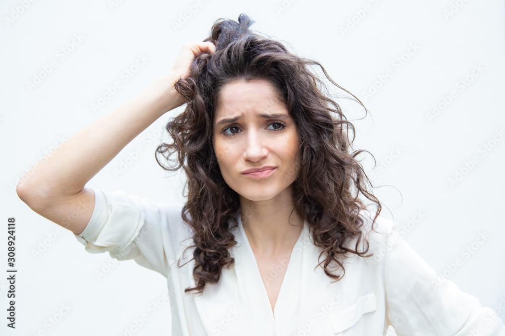 Worried pensive woman scratching head and looking away. Wavy haired young woman in casual shirt standing isolated over white background. Hard decision making concept Worried pensive woman scratching head and looking away. Wavy haired young woman in casual shirt standing isolated over white background. Hard decision making concept