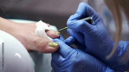The toes are separated. The master is applying the green nail polish. The pedicure technician is performing in rubber gloves to protect herself from infection. photo