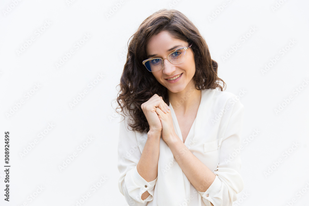 Positive female professional with clasped hands smiling at camera. Wavy haired young woman in casual shirt standing isolated over white background. Female portrait concept Positive female professional with clasped hands smiling at camera. Wavy haired young woman in casual shirt standing isolated over white background. Female portrait concept
