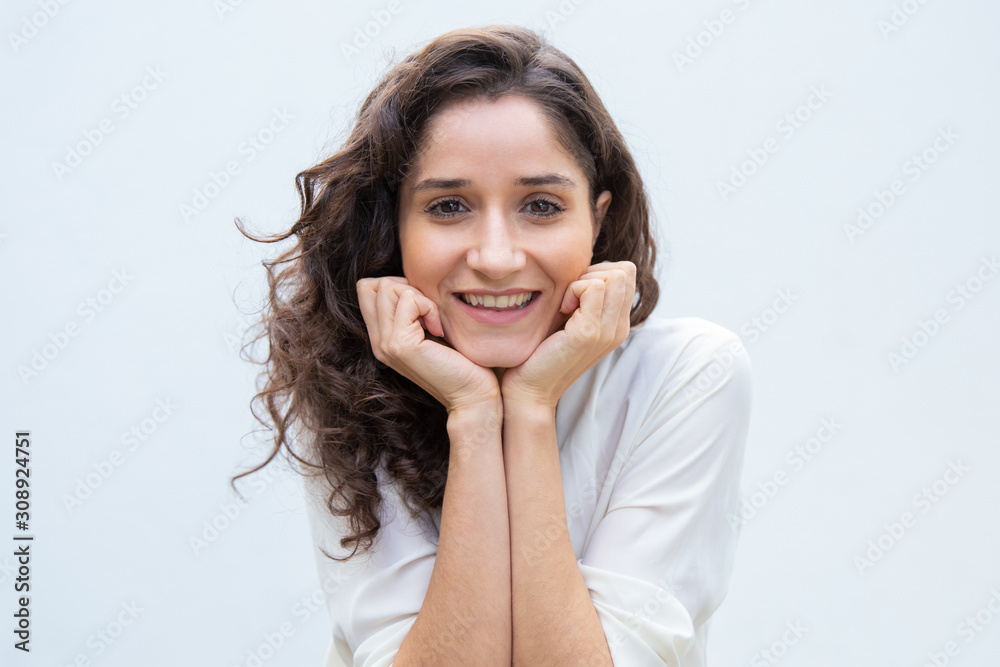 Happy beautiful student girl leaning chin and head on hands, smiling, looking at camera. Wavy haired young woman in casual shirt standing isolated over white background. Female portrait concept Happy beautiful student girl leaning chin and head on hands, smiling, looking at camera. Wavy haired young woman in casual shirt standing isolated over white background. Female portrait concept