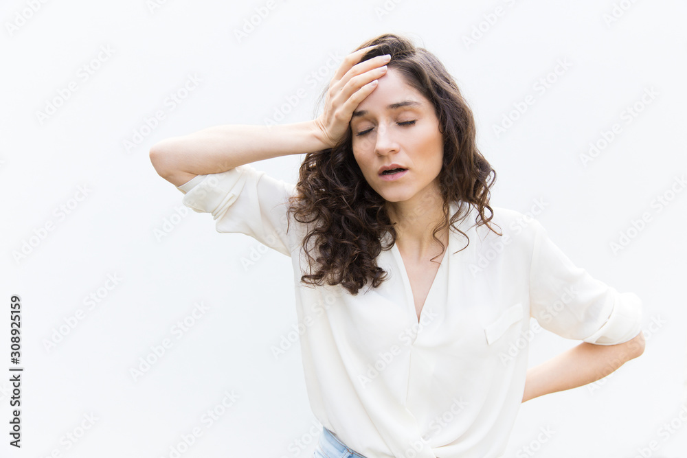 Exhausted tired woman with closed eyes touching head. Wavy haired young woman in casual shirt standing isolated over white background. Headache or burnout concept Exhausted tired woman with closed eyes touching head. Wavy haired young woman in casual shirt standing isolated over white background. Headache or burnout concept