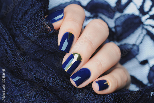 Deep blue manicure with gold design elements stripes and triangle. Blue lace background