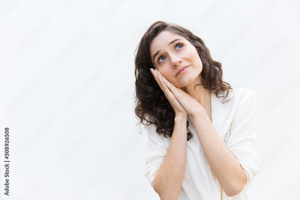 Positive woman making sleep gesture and looking up at copy space. Wavy haired young woman in casual shirt standing isolated over white background. Advertising concept Positive woman making sleep gesture and looking up at copy space. Wavy haired young woman in casual shirt standing isolated over white background. Advertising concept