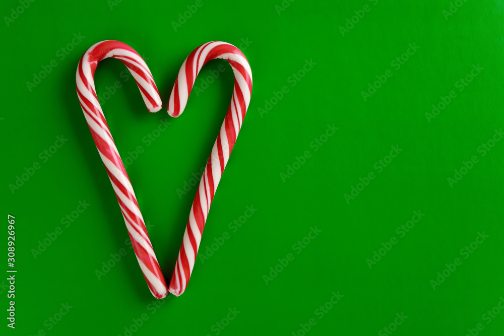 Two christmas red and white candy canes in the shape of heart on a green paper background. Two christmas red and white candy canes in the shape of heart on a green paper background.