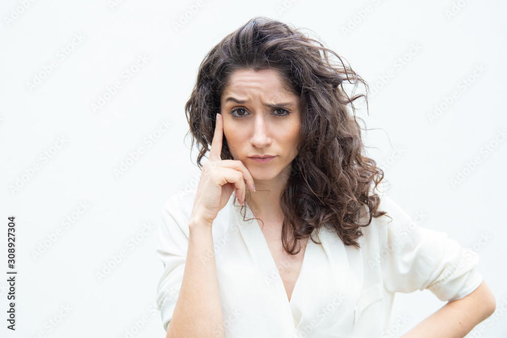 Pensive focused female customer touching face with finger, looking at camera, thinking. Wavy haired young woman in casual shirt standing isolated over white background. Decision making concept Pensive focused female customer touching face with finger, looking at camera, thinking. Wavy haired young woman in casual shirt standing isolated over white background. Decision making concept