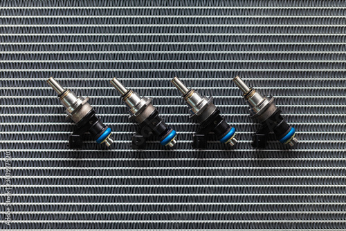 Auto Parts - four fuel nozzles of the injector for the combustion chamber of the engine lie against the background of the patterns of the cooling radiator.