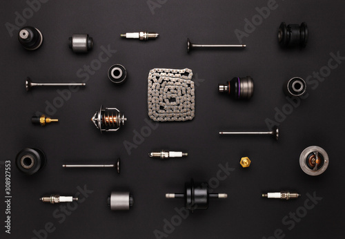 Studio photography - a lot of automotive parts: valves, spark plugs, silent blocks, thermostats, filter, sensors, chain, ball bearings, lie in straight rows on a flat surface isolated on a black 