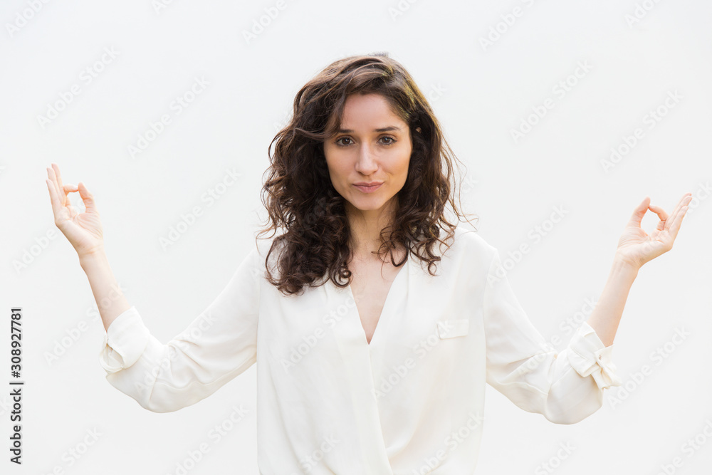 Positive female yogi making zen gesture with hands. Wavy haired young woman in casual shirt standing isolated over white background. Meditation concept Positive female yogi making zen gesture with hands. Wavy haired young woman in casual shirt standing isolated over white background. Meditation concept