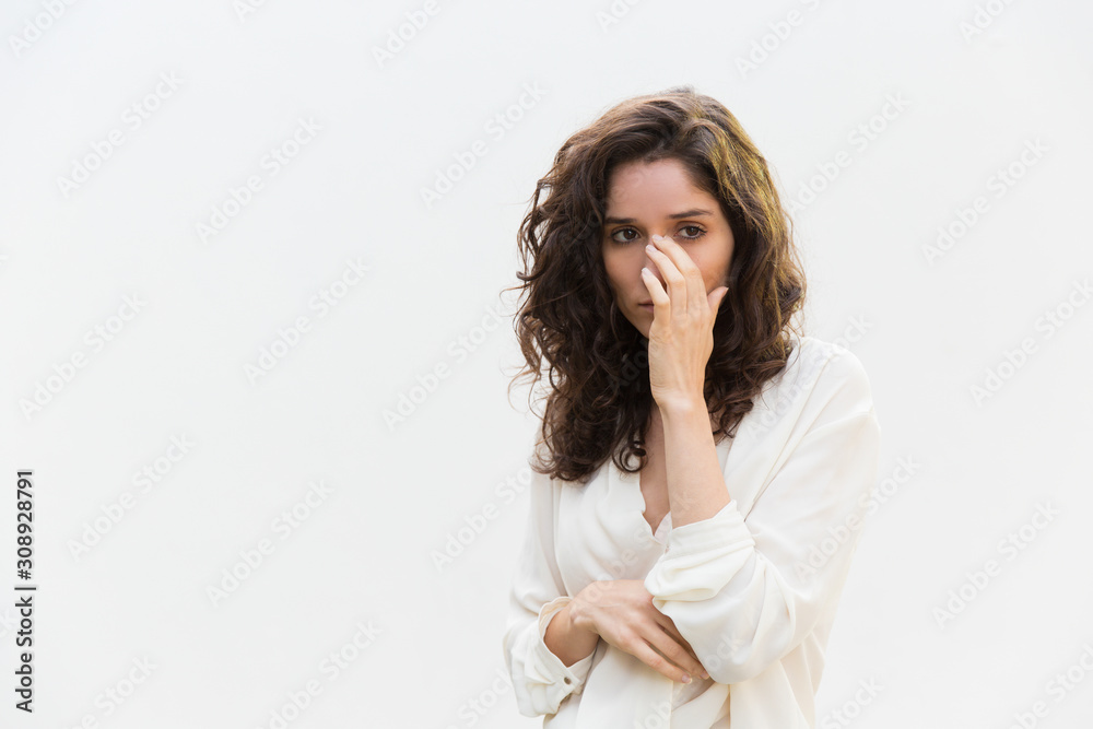Upset frustrated crying woman removing tears from face, looking away. Wavy haired young woman in casual shirt standing isolated over white background. Bad news concept Upset frustrated crying woman removing tears from face, looking away. Wavy haired young woman in casual shirt standing isolated over white background. Bad news concept