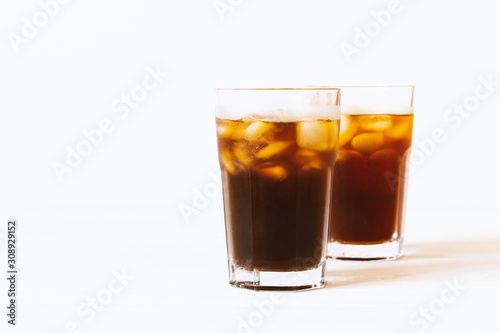 Black tea, coffee or cola with ice in glass on white background. Horizontal photo with copy space. Two glass with drink on table. Summer beverage