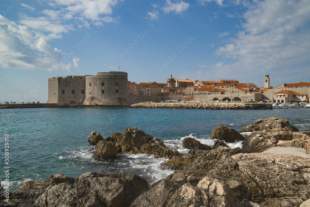 Rocky beach and sea waves on the background of ancient town with fortress