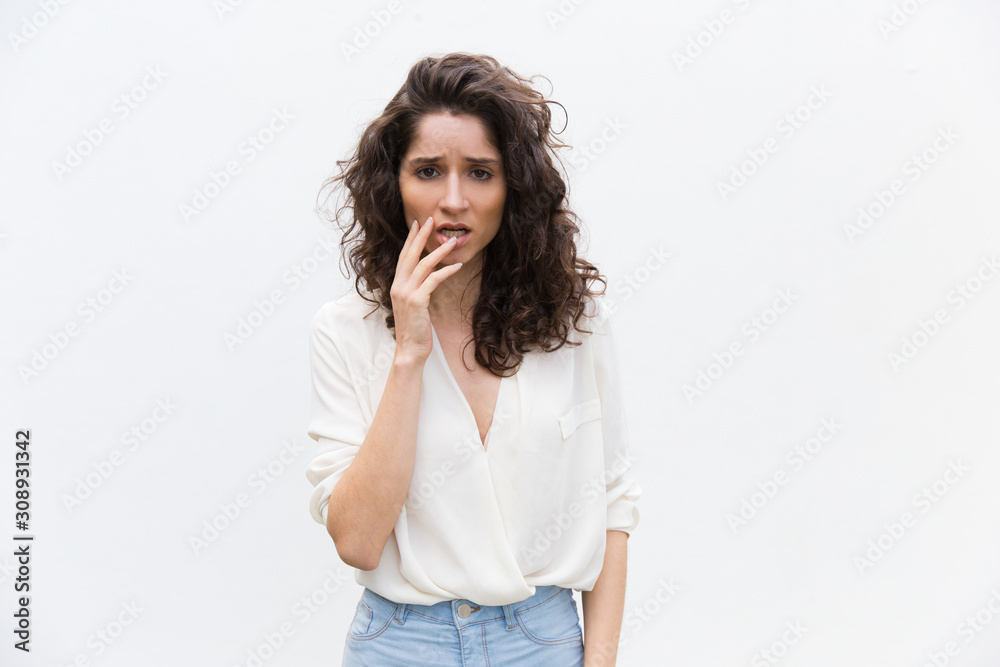 Worried confused woman touching face, realizing mistake. Wavy haired young woman in casual shirt standing isolated over white background. Error or memory problem concept Worried confused woman touching face, realizing mistake. Wavy haired young woman in casual shirt standing isolated over white background. Error or memory problem concept