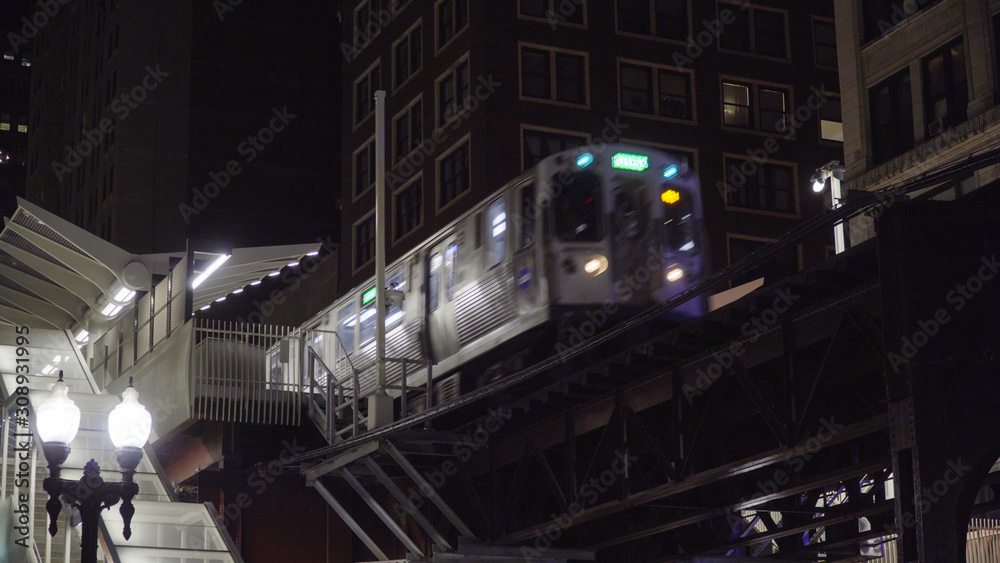 Night time exterior of loop train passing through elevated station on tracks through downtown chicago during dark evening rush hour commute Night time exterior of loop train passing through elevated station on tracks through downtown chicago during dark evening rush hour commute