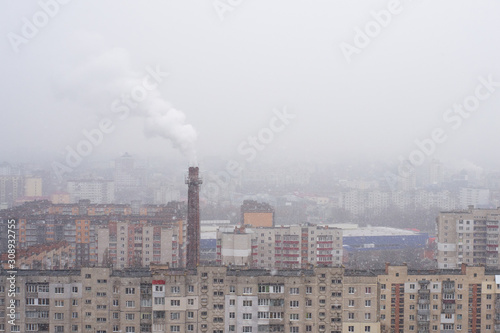 Smoking chimney of a thermal power plant on the background of a snowing city