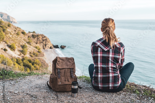 Young hip woman with a backpack explores the coast on a beautiful day. Concept of exploration and adventures