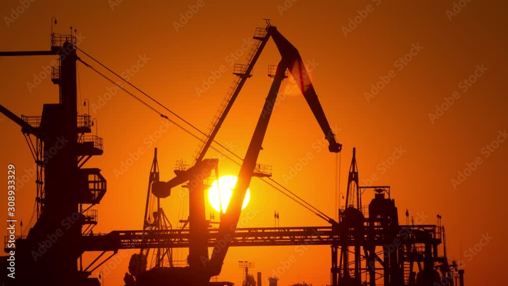 Time-lapse of solar disk moving behind working port cranes silhouette Time-lapse of solar disk moving behind working port cranes silhouette