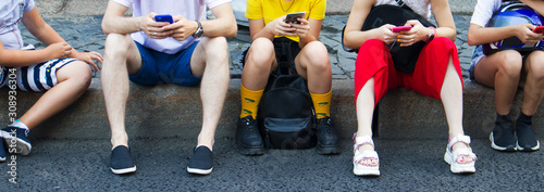 Group of teenagers sitting with phones on the sidewalk 