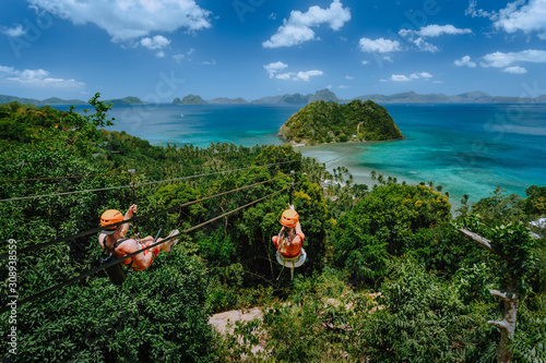 Zipline over Las Cabanas Beach with tourist on sunny day with white clouds over sea. El Nido, Palawan, Philippines