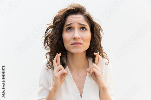 Anxious woman keeping fingers crossed and praying for luck. Wavy haired young woman in casual shirt standing isolated over white background. Making wish concept photo
