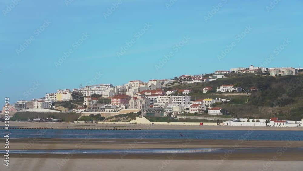 Lagoa Obidos Portugal - A Man Kite Surfing Across The Sea With The Cityscape At The Background - Wide Shot Lagoa Obidos Portugal - A Man Kite Surfing Across The Sea With The Cityscape At The Background - Wide Shot