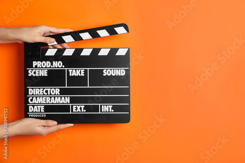 Tableau sur toile Woman holding clapperboard on orange background, closeup with space for text