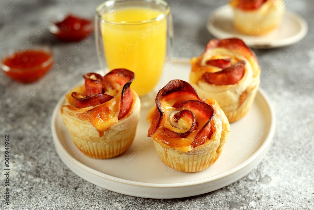 Muffins roses from puff pastry with ham and cheese on a light background.