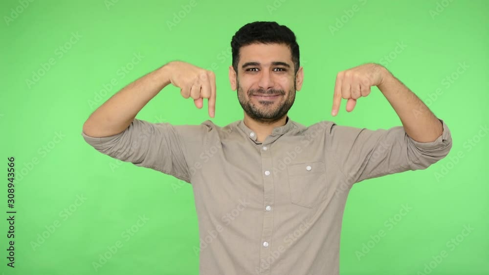 Look down, subscribe! Excited happy brunette man in shirt pointing down and nodding approvingly, pointing to camera, advertising area for promotional text. studio shot, green background, chroma key