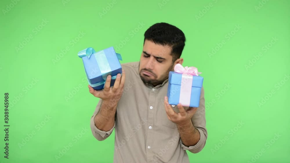 Embarrassed man in shirt holding two wrapped gifts, shaking boxes and listening to guess what's inside, looking inquiring confused, no idea what is present. studio shot, green background, chroma key Embarrassed man in shirt holding two wrapped gifts, shaking boxes and listening to guess what's inside, looking inquiring confused, no idea what is present. studio shot, green background, chroma key