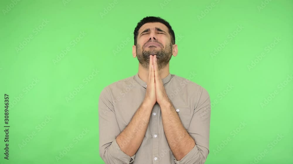 Distressed brunette man with bristle in shirt clasping hands in prayer, looking up with pleading expression and begging forgiveness, feeling desperate helpless. studio shot, green background, chroma Distressed brunette man with bristle in shirt clasping hands in prayer, looking up with pleading expression and begging forgiveness, feeling desperate helpless. studio shot, green background, chroma
