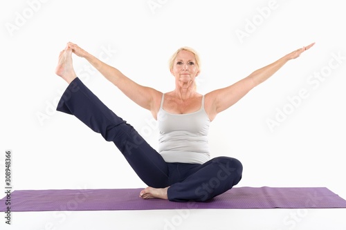 Mature woman sitting on mat and doing yoga with arms outstretched