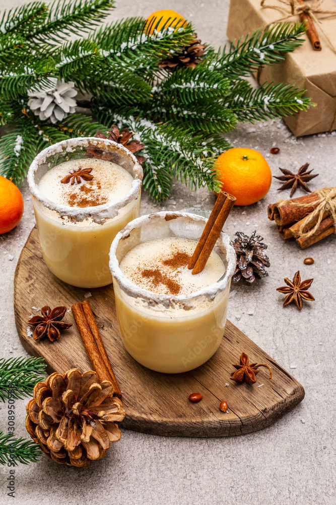 Eggnog with cinnamon and nutmeg for Christmas and winter holidays. Homemade beverage in glasses with spicy rim. Tangerines, candles, gift. Stone concrete background Eggnog with cinnamon and nutmeg for Christmas and winter holidays. Homemade beverage in glasses with spicy rim. Tangerines, candles, gift. Stone concrete background