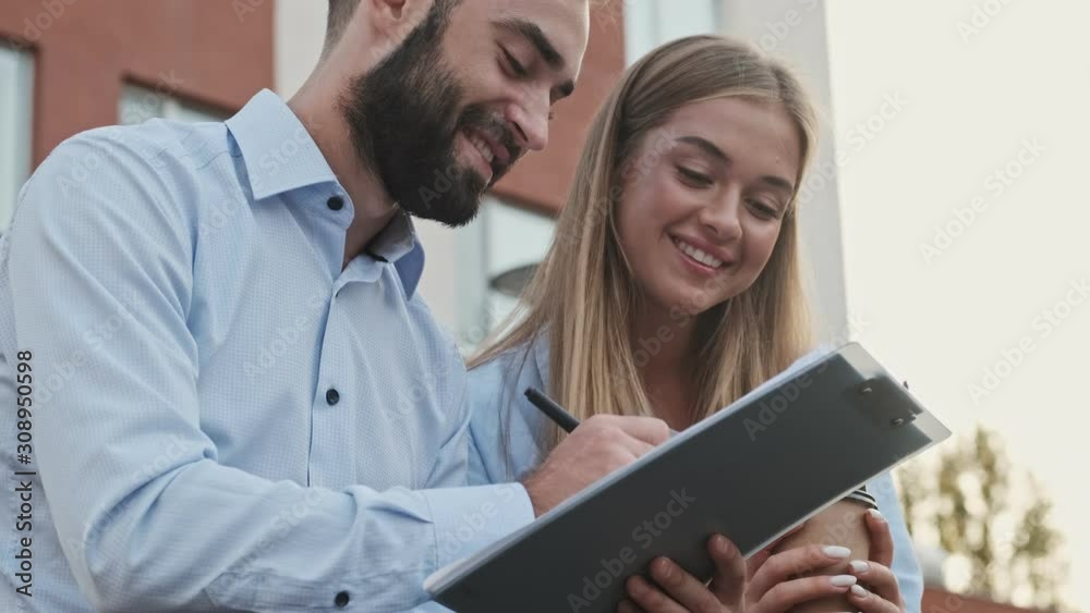 Close up view of Happy young office colleagues checking something in clipboard while sitting outdoors Close up view of Happy young office colleagues checking something in clipboard while sitting outdoors