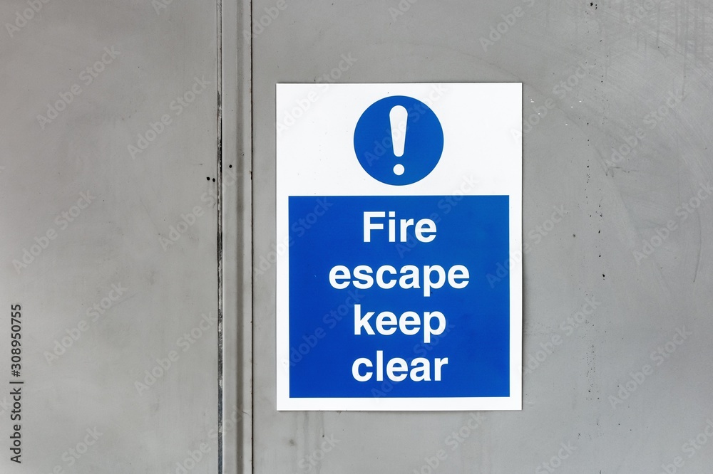 The sign Fire escape Keep clear on a grey metal door warning other not to stay in this hazardous zone The sign Fire escape Keep clear on a grey metal door warning other not to stay in this hazardous zone