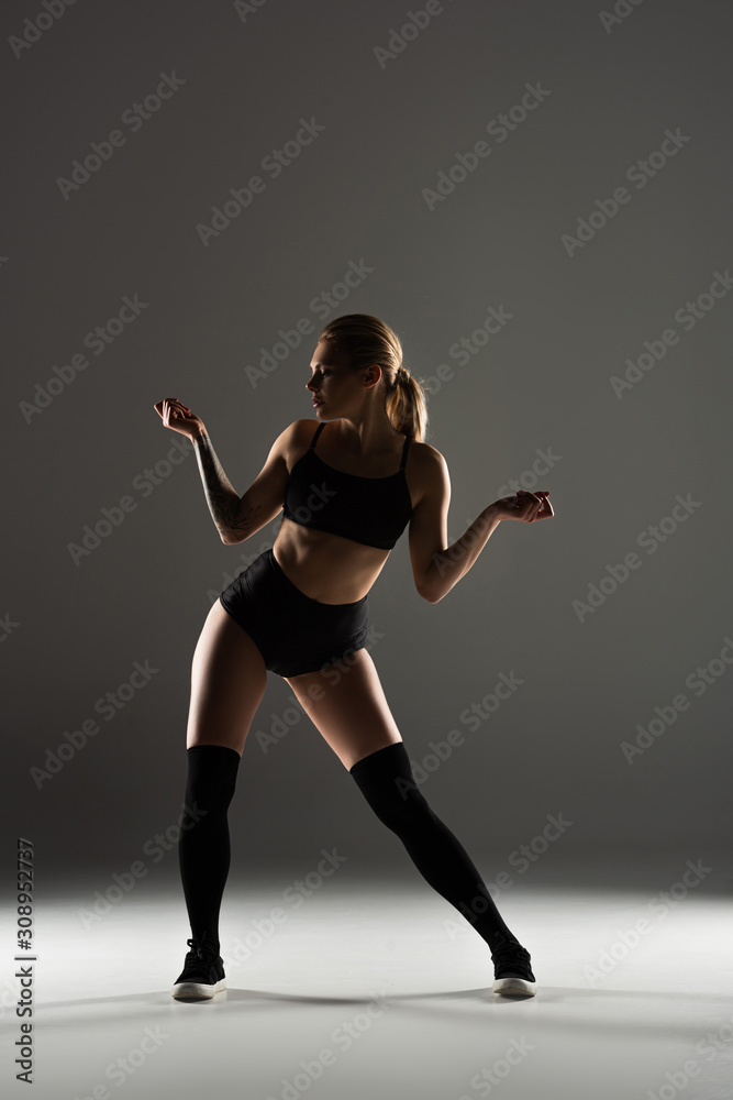 sexy girl in black outfit  twerking in shadow on grey background