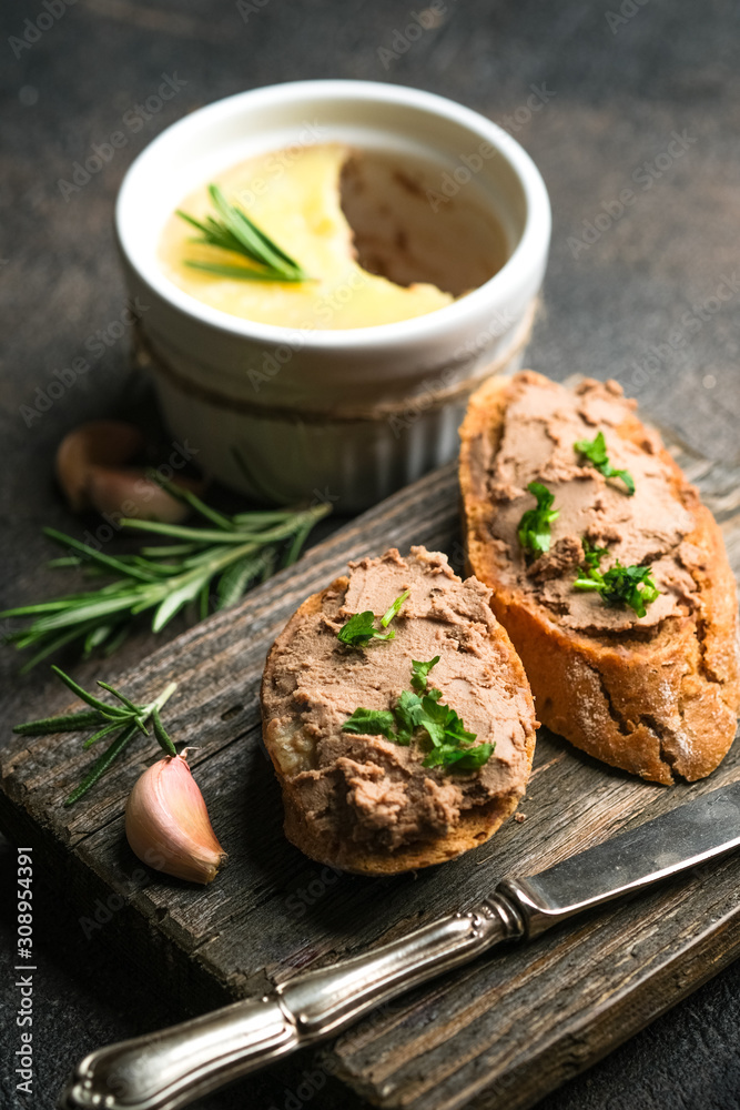 Fresh homemade chicken liver pate in ceramic bowl or ramekin and baguette slices with pate on the serving board, selective focus.