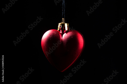 Red Christmas bauble over dark background. Low key photo. Heart shape.