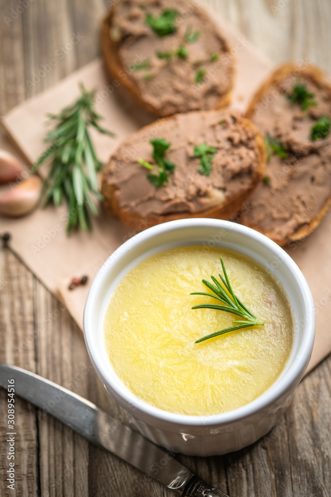 Fresh homemade chicken liver pate in ceramic bowl or ramekin and baguette slices with pate with herbs and garlic on a rustic wooden background. Top view. Fresh homemade chicken liver pate in ceramic bowl or ramekin and baguette slices with pate with herbs and garlic on a rustic wooden background. Top view.