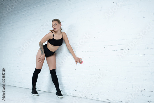 tattooed sexy blonde girl in black outfit twerking near wall in studio © LIGHTFIELD STUDIOS