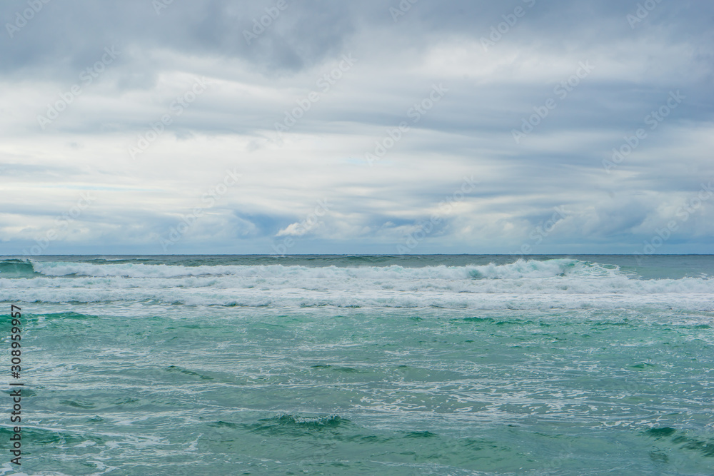 Waves at the coast. Stormy weather with a clouded grey sky and a rolling turquoise ocean. The shore at Unstadt Beach, Vestvågøy, Lofoten Islands, Norway.