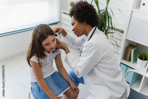 Woman afro american doctor general practitioner examining ear of a ill child. Ear infections. photo