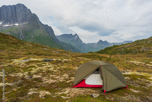 Open tent in green and red colors standing in wild landscape with mountain tops in the background. Autumn weather and clouds on the sky. Senja, Norway.